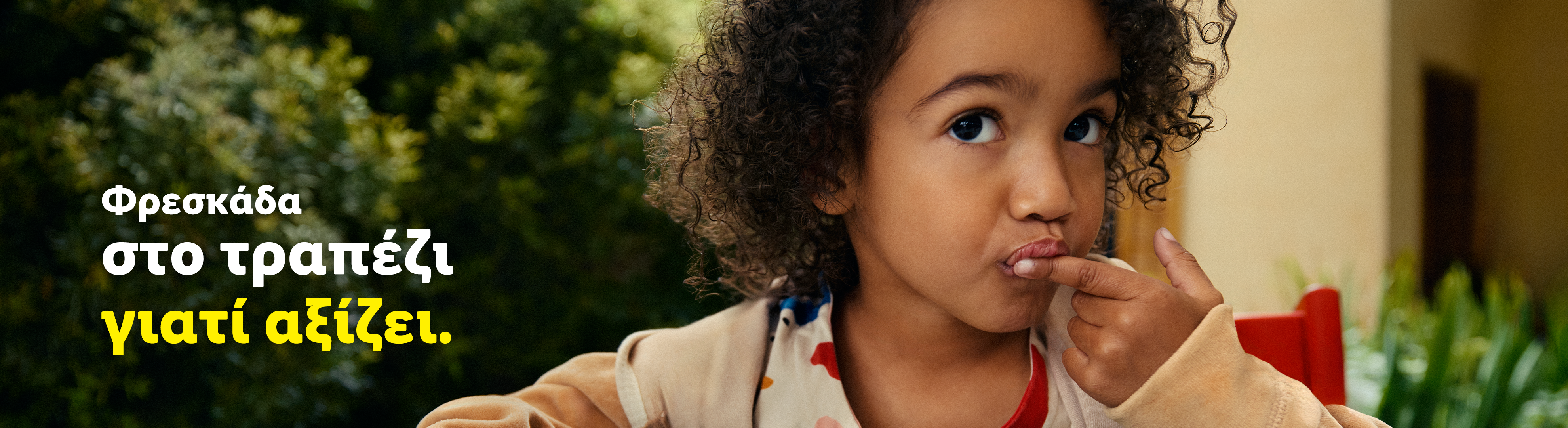Ένα παιδί με σγουρά μαλλιά κοιτάζει την κάμερα, με κείμενο «Φρεσκάδα στο τραπέζι γιατί αξίζει».